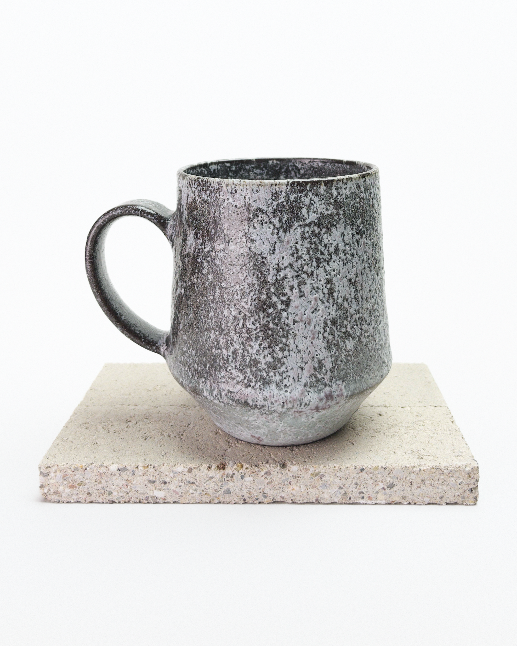 A large gray, shino-glazed mug with moss-like, white glaze patches. Front view with handle to the left.