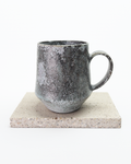 A large gray, shino-glazed mug with moss-like, white glaze patches. Back view with handle to the right.