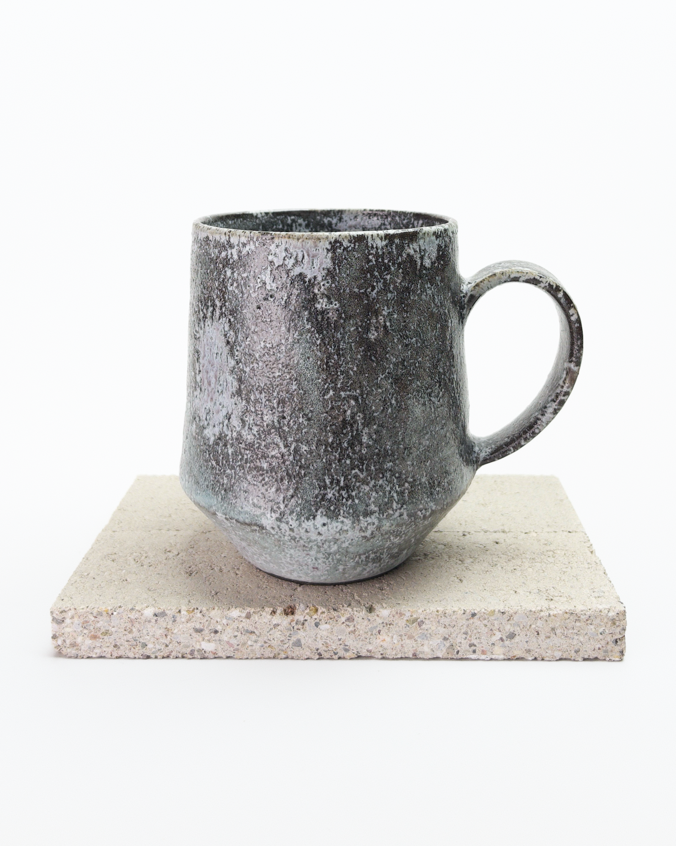 A large gray, shino-glazed mug with moss-like, white glaze patches. Back view with handle to the right.