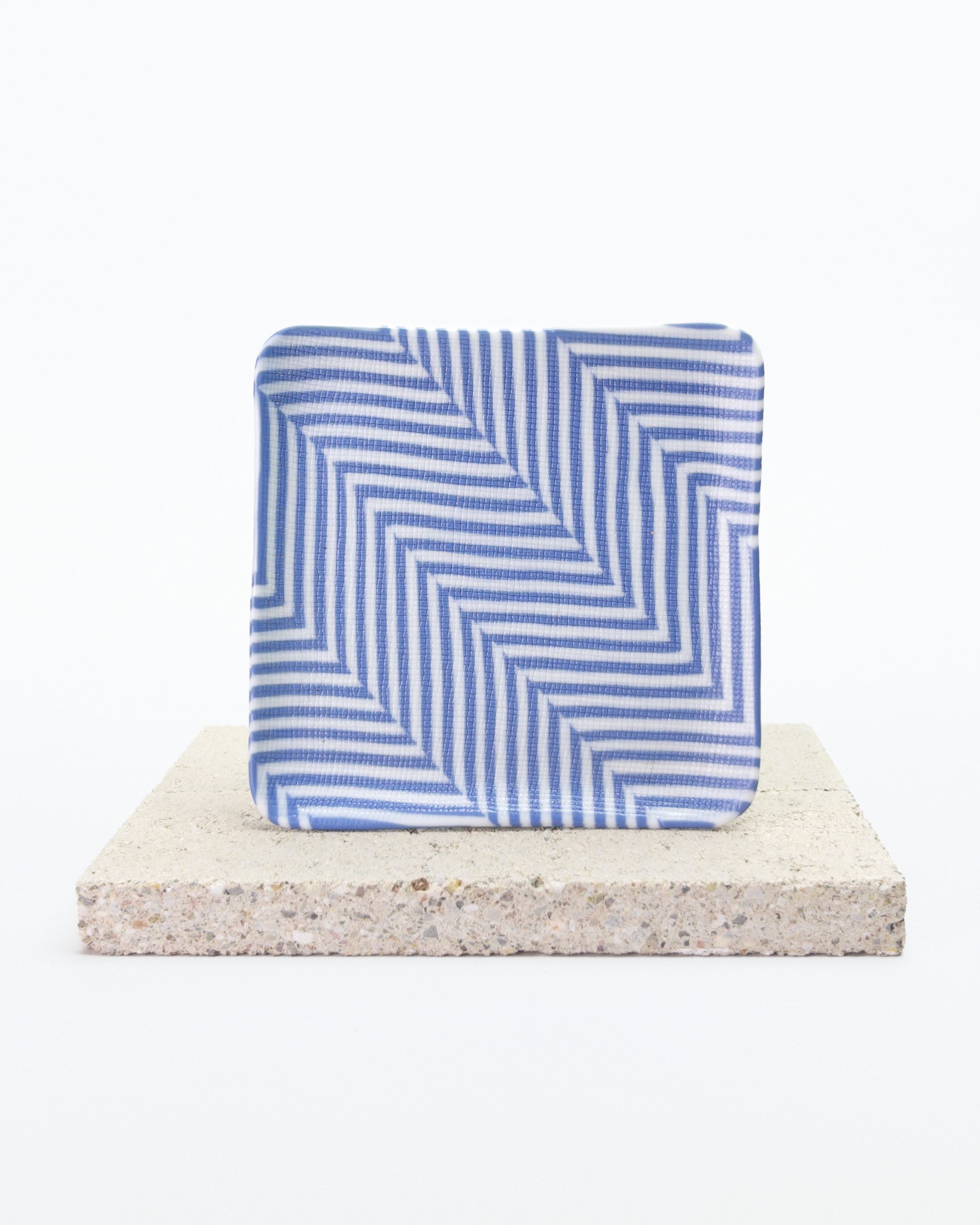Front side of blue and white striped nerikomi plate with on a beige stone surface