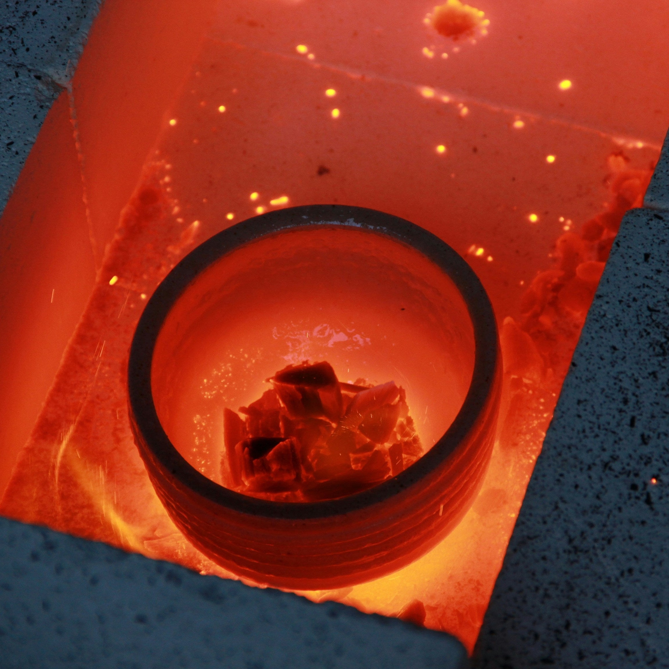 Ceramic tea bowl being fired in an open kiln with glowing red-hot interior.